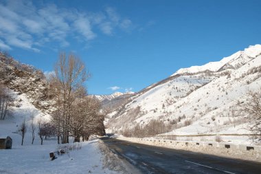 Karlı dağlarda bir yolu olan kış manzarası ve mavi gökyüzünün arka planına sahip vadi. 