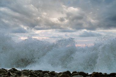 Büyük köpüklü su sıçrayan deniz dalgası çakıl taşı plajını eziyor.
