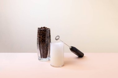 Pembe şeftali arka planında bir bardak sütle süt köpüğü üreticisi..