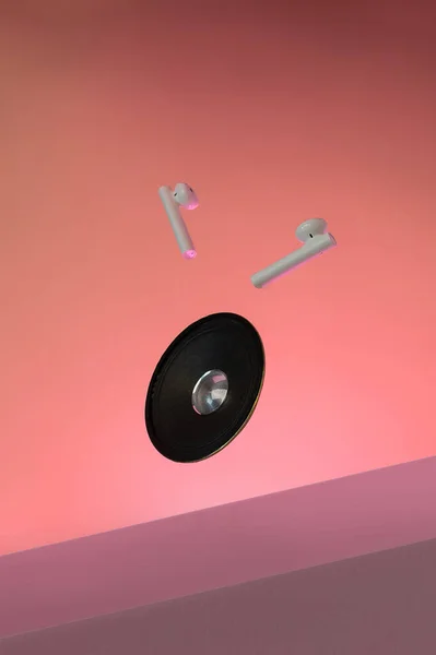 Earphones bluetooth, speaker levitation on pink background.