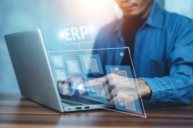 ERP yazılım belgesi kavramı, belge yönetimi kavramı. Sanal ekranda ve ofis geçmişinde simgeleri olan dizüstü bilgisayarla çalışan bir iş adamı.