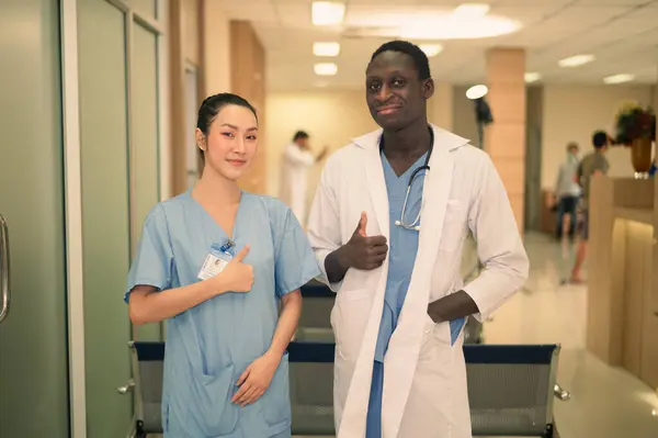 Asian and American doctor Successful team of medical doctors are looking at camera and smiling while standing in hospital.