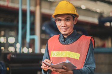 Asyalı mühendis endüstriyel bir fabrikadaki makineleri özenle inceliyor. Sanayi fabrikalarında odaklanmış olan makineleri özenle denetliyor..