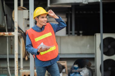 Asyalı mühendis endüstriyel bir fabrikadaki makineleri özenle inceliyor. Sanayi fabrikalarında odaklanmış olan makineleri özenle denetliyor..