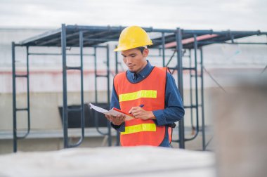 Asyalı mühendis endüstriyel bir fabrikadaki makineleri özenle inceliyor. Sanayi fabrikalarında odaklanmış olan makineleri özenle denetliyor..