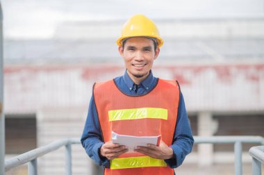 Asyalı mühendis endüstriyel bir fabrikadaki makineleri özenle inceliyor. Sanayi fabrikalarında odaklanmış olan makineleri özenle denetliyor..