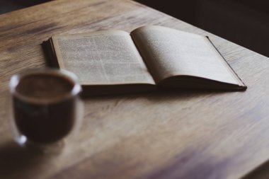 Bir fincan kahve ve açık bir kitap. Kahve fincanı ve ahşap masada eski bir kitap. Edebiyat konsepti. Sonbahar hala hayattır. Kütüphanede Espresso. Bilgi ve bilgelik. İçerisi sıcacık. Bir bardak kahve ve kitap..