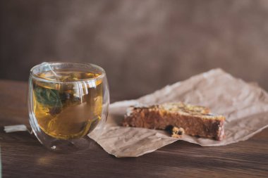 Bardakta bitki çayı ve kağıtta bisküvi. Sıcak bir kahvaltı. Bardakta çay poşeti ve pasta. Sıcak içecek ve tatlı. Kafede taze fırın ve çay.. 