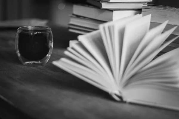 Stack of old books and coffee cup, black and white. Literature background. Open book and pile of books on the table. Coffee time in library. Retro books and espresso. Wisdom and knowledge.