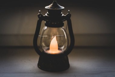 Geceleyin eski bir gaz lambası. Siyah arka planda klasik fener. Akşamları dekoratif lamba. Ukrayna 'da elektrik kesintisi. İç mekan. Karanlıkta parlayan mum ışığı. Küçük bir gaz lambası. Yıllanmış fener.