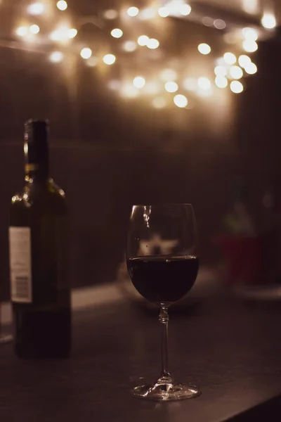 Glass of red wine and bottle at the table. Evening still life. Red wine in bar. Alcohol drinks concept. Wineglass and bottle of red wine in restaurant. Cozy evening with drinks.