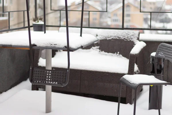 Outdoor furniture covered with snow. Snow covered chairs and sofa on balcony. Winter in the city. Town covered with fresh snow. Frozen town. Outdoor cafe in snowy winter. Snowy weather.