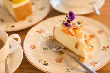 Piece of decorated cheesecake on plate with fork. Breakfast in vintage style. Cheesecake with flaked almonds and coffee. Handmade cake on table. Sweet dessert concept. Creamy cake and coffee cup. Cafeteria concept.