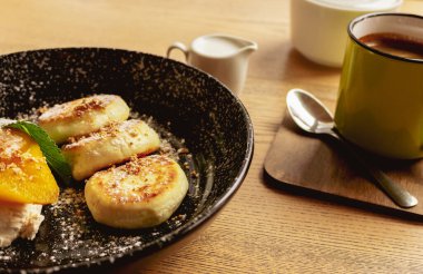 Karamelli armut ve kahve fincanlı Syrniki. Sütlü ve sütlü krep. Nefis bir kahvaltı. Ukrayna yemeği. Peynirli krep ve bir fincan kahve. Restoran menüsü. Ev yapımı tatlı..