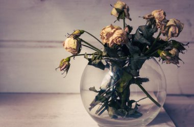 Işık ve gölgede eskimiş gül buketi. Vazoda küçük kuru güller. Beyaz çiçekler kapanıyor. Solma konsepti. Ayrılma konsepti. Üzücü aşk konsepti. Çıkmak için çiçekler. Camdaki güller, eski tarz..