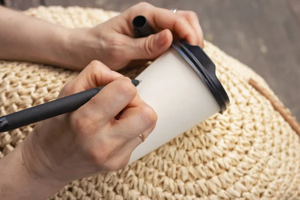 白いカップの上に女性が言葉を描く コーヒーを手に持ってカップを奪う 白い紙コップがモックアップ 工芸の概念 コピースペース付きコーヒーカップ — ストック写真
