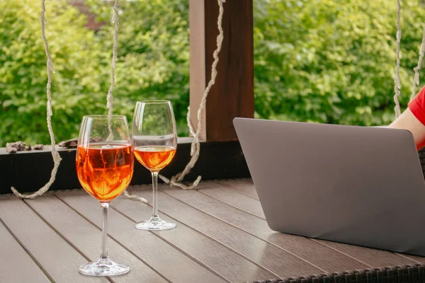 İçinde bir bardak Aperol kokteyli olan dizüstü bilgisayar. Açık kafede kablosuz bilgisayarla çalışan bilinmeyen biri. Halka açık bir yerde serbest çalışan. Gri dizüstü bilgisayar ve masada iki bardak şarap. Huzurlu tatiller. 