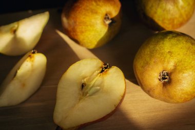 Pears on wooden table in sunlight. Ripe pears and slices of pears on wooden board. Juicy fruits. Autumn farming. Autumn harvest. Raw food. Slices of sweet pear. Organic fruits. 