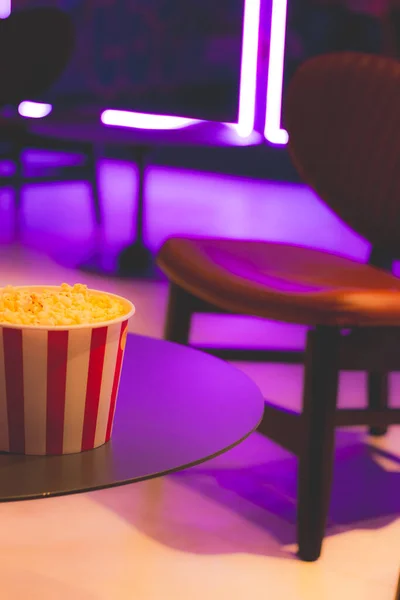 Popcorn box in neon lights. Movie theatre popcorn background. Entertainment concept. Cinema trendy. Movie snack. Salted popcorn in bucket. Fast food.
