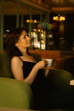 Kafede kahve içen güzel bir kadın. Günlük hayat konsepti. Hayat konseptinin tadını çıkar. Kanepede bir fincan çayla esmer bir kız. Rahat bir yaşam tarzı. Kafenin içindeki güzel kadın. Kahve molası. Büyük şehir hayatı. Kurulum arkaplanı.