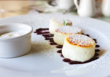 Kiraz reçeli ve ekşi kremalı süzme peynirli krep. Beyaz tabakta vanilya şurubu. Tatlı peynirli tatlı. Güzel kahvaltı konsepti. Kafede reçelle süslenmiş peynirli tatlı.. 