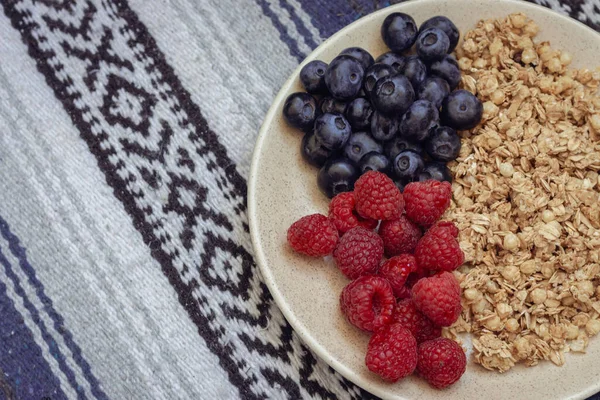 Masa örtüsünde yabanmersini ve ahududu olan müsli. Havlu desenli yaban mersinli granola. Sağlıklı beslenme. Bir kase yulaf gevreği, yabanmersini ve ahududu. Vitamin kahvaltısı. Mısır gevreği ve böğürtlen.. 