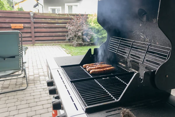 Sausages on the grill. Garden barbecue party. Pork sausages on the grill grate. Grilled bratwurst sausages. Picnic at backyard. Hot dog cooking. Unhealthy food. BBQ food concept.