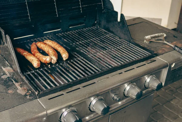 Sausages on the grill. Garden barbecue party. Pork sausages on the grill grate. Grilled bratwurst sausages. Picnic at backyard. Hot dog cooking. Unhealthy food. BBQ food concept.