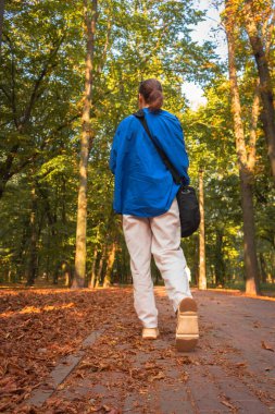 Sonbahar parkında arkada yürüyen kız. Sonbahar macerası. Ormanda iz süren bir kadın. Sonbahar manzarası ve turist. Sonbahar parkında sakin, güneşli bir hava. Doğa keşfi. Aktif yaşam tarzları. Kırsalda yürüyüş..