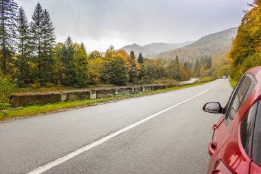 Sonbahar dağlarında kırmızı araba yolda. Ukrayna 'da, Karpat dağlarında seyahat et. Virajlı otoyoldaki araba muhteşem bir orman arka planında. Hafta sonu araba yolculuğu. Sonbahar dağlarında araba sürmek. Seyahat hedefleri kavramı. 