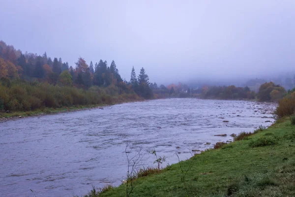 Fog on the river in autumn mountains. Frosty morning in mountains at the riverside. Tranquil autumn landscape with river. Scenic misty countryside. Travel in Carpathian autumn village.