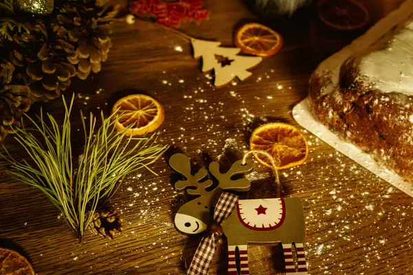 Christmas background with elk toy, dried orange fruit and festive lights. Advent decoration. New Year eve celebration. Christmas card. Winter holidays table. Christmas garland lights with sweet stollen.