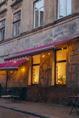 Ukrayna 'nın eski Lviv kasabasındaki kafe pencerelerinde sıcak ışıklar. Dışarıdaki mobilyaları ve pencerelerinde çelengi olan bir kafe. Antik evdeki kaldırım kafesi. Restoranın dışı. Şehir yaşam tarzı. 