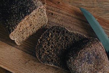 Tahtada bıçak olan gri ekmek. Tahtada buğday ekmeği dilimleri. Fırın ürünleri. Masada kabuklu tahıllı ekmek. Yemek konsepti. Sağlıklı beslenme tarzı. Taze mısır gevreği. Taze gıda konsepti. 