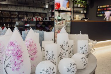 Masada beyaz boyalı mumlar. Mum dükkanı. Ev aletleri. Dükkanda farklı mumlar var. Aroma mumları. Aşk aksesuarları. Çeşitli mum yığınları.