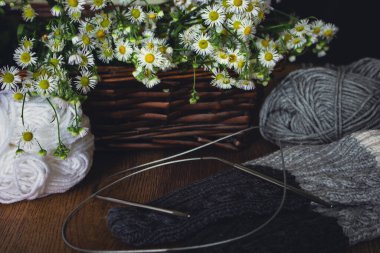 İplik topları ve örgü çoraplar. Tahta masanın üzerinde beyaz demetler var. Örgü hobisi. Gri ve beyaz yün iplik ve sıcak çoraplı örgü iğneleri. İçerisi sıcacık. İğne işi konsepti. El işi yaratıcılığı.