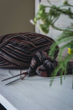 Küçük demetler ve örgü iğneli çizgili yün iplik. Papatya çiçeği ve dikiş işi. Beyaz ahşap rafta rahat örülmüş çoraplar. Kırsal yaşam tarzı. Papatya çiçekleri ve örgü.. 