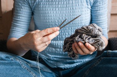 Mavi elbiseli kadın elinde gri iplik yumağı ve örgü iğneleri tutuyor. Ellerinde dikiş iplikleri ve iğnelerle oturan bir kız. Örgü konsepti. Yaratıcı bir yaşam tarzı. Örgü hobisi. El işi ilhamı.