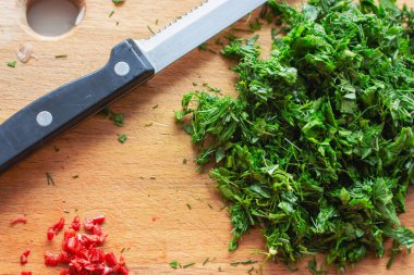 Tahta tahtada bıçakla doğranmış maydanoz ve biber yığını. Doğranmış yeşil otlar ve kırmızı biber. Sağlıklı beslenme konsepti. Çiğ gıda geçmişi. Ev yemeği arka planı. 