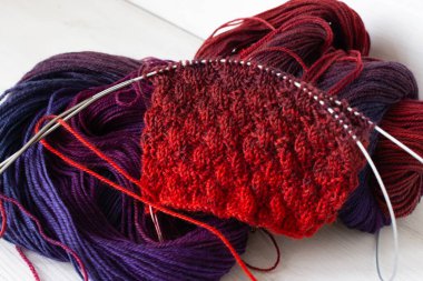 Örgü ve iğneli parlak renkli iplik yumağı. Güzel örgü desenli parlak eğimli iplikler. Beyaz arka planda kırmızı ve menekşe tığ işi. Örgü hobisi. Örgü giyme konsepti. İğne işi arkaplanı. 