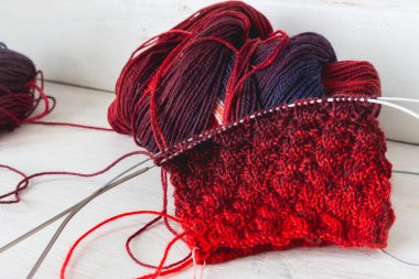 Örgü ve iğneli parlak renkli iplik yumağı. Güzel örgü desenli parlak eğimli iplikler. Beyaz arka planda kırmızı ve menekşe tığ işi. Örgü hobisi. Örgü giyme konsepti. İğne işi arkaplanı. 