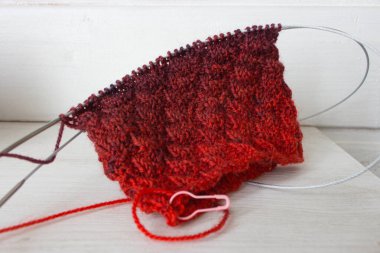 Örgü ve iğneli parlak renkli iplik yumağı. Güzel örgü desenli parlak eğimli iplikler. Beyaz arka planda kırmızı ve menekşe tığ işi. Örgü hobisi. Örgü giyme konsepti. İğne işi arkaplanı. 