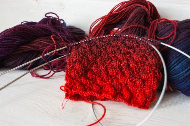 Örgü ve iğneli parlak renkli iplik yumağı. Güzel örgü desenli parlak eğimli iplikler. Beyaz arka planda kırmızı ve menekşe tığ işi. Örgü hobisi. Örgü giyme konsepti. İğne işi arkaplanı. 