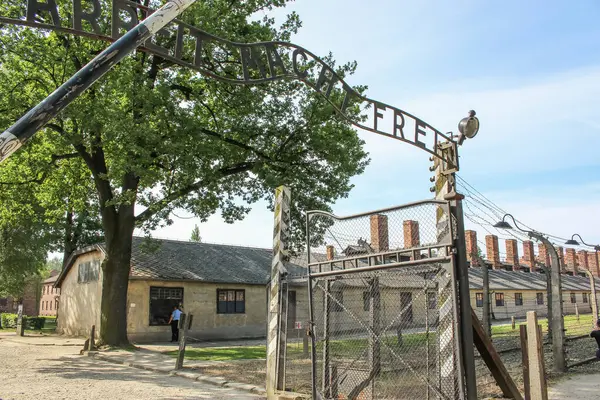 stock image Poland, Oswiecim - 06 15 2018: Gate to concentration camp Auschwitz, Oswiecim. Entrance with nazi slogan and barrack on background. Holocaust memorial. Symbol of fascism violence. Jewish genocide. Death camp museum. Nazi prison. Jail concept. 