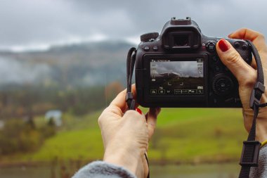 Yağmurlu bir günde dağlarda fotoğraf çeken bir fotoğrafçı. Kadınların elinde sonbahar doğasına odaklı kamera. Fotoğraf hobisi. Kamera önünde sonbahar kırsalında. Karpat dağlarında macera, Ukrayna.