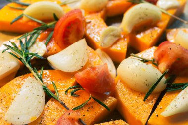 Soğan, sarımsak ve biberiye yapraklı dilimlenmiş balkabağı. Sonbahar yemekleri hala hayattadır. Çiğ balkabağı dilimleri, bitkiler ve baharatlar, yakın çekim. Sağlıklı beslenme konsepti. Vejetaryen yemeği. Diyet yemek..