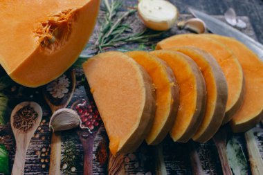 Kesme tahtasının üzerinde soğanlı, sarımsaklı ve biberiyeli balkabağı. Sonbahar yemekleri hala hayattadır. Çiğ balkabağı dilimleri, bitkiler, baharatlar ve bıçaklar, yakından. Sağlıklı beslenme konsepti. Vejetaryen yemeği. Diyet yemek..