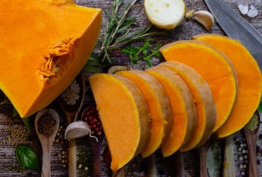 Kesme tahtasının üzerinde soğanlı, sarımsaklı ve biberiyeli balkabağı. Sonbahar yemekleri hala hayattadır. Çiğ balkabağı dilimleri, bitkiler, baharatlar ve bıçaklar, yakından. Sağlıklı beslenme konsepti. Vejetaryen yemeği. Diyet yemek..