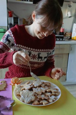 Noel süveteri içinde gülümseyen kadın zencefilli kurabiye yapıyor. Kış tatili için pudra şekerli kurabiye süsleyen mutlu kız. Noel ziyafeti yemekleri. Rahat ev hayatı..
