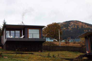 Sonbahar dağlarında sabahları bulutlarla kaplı lüks evler. Ukrayna 'daki Karpat Dağları' nda modern bir otel. Dağlık bölgede sisli bir sabah. Sisli tepelerdeki sonbahar ormanında bir ev. Eko turizm konsepti. Sonbahar havası.